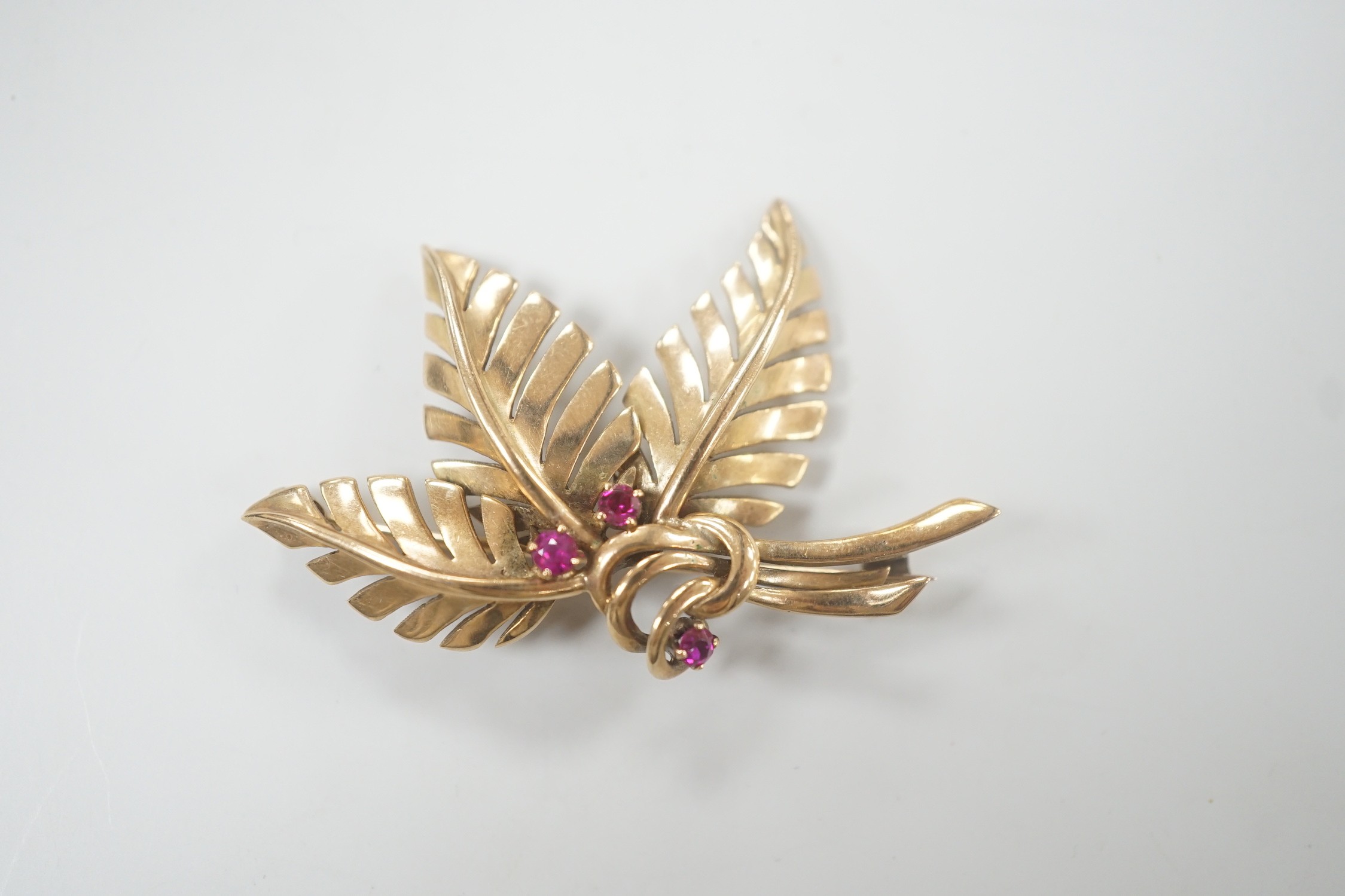 A yellow metal and three stone ruby set foliate brooch, 45mm, gross weight 6.8 grams.